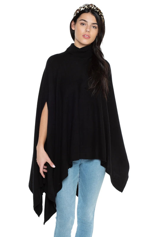 Woman wearing the JENNIE LIU black cashmere poncho, an oversized sleeveless cowl neck poncho with an asymmetric hem, over light blue jeans